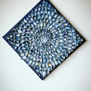 May include: A square canvas painting with a blue and white abstract design. The design is made up of many small, overlapping shapes that create a swirling, organic pattern.