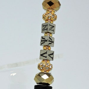 May include: A black pen with a silver tip and a decorative top made of gold and silver beads with rhinestones. The beads spell out the word "NAVY".