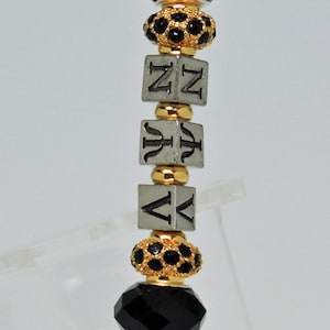 May include: A gold pen with black and gold beads and a silver charm with the letters "NVN" on it.