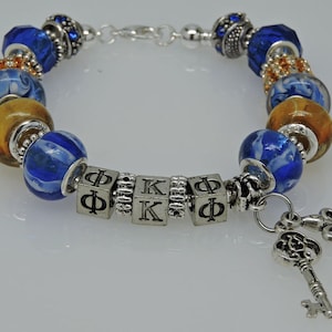 May include: A silver charm bracelet with blue and gold beads, including a charm with the letters "ΦΚΦ" and two key charms.