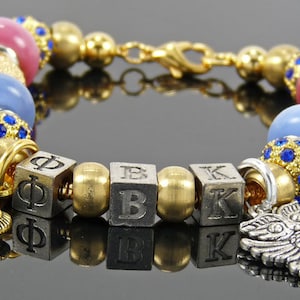 May include: A gold charm bracelet with blue and pink beads, gold and silver charms, and a silver charm with a fleur-de-lis design. The bracelet has a silver charm with the letters "ΦΒΚ" on it.