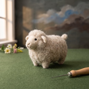 May include: A needle-felted sheep figurine crafted from textured, off-white wool fibers. The small animal sculpture features a rounded body, a detailed face with dark eyes, and a small tail, standing upright on a flat, green surface.
