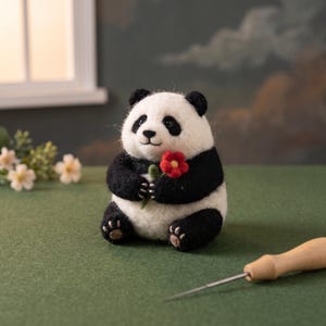 Könnte beinhalten: Eine nadelgefilzte Panda-Figur aus schwarzer und weißer Wolle, die in aufrechter Position sitzt. Der Panda hat schwarze Ohren, Augenpartien, Arme und Beine und hält eine kleine rote Blume mit gelber Mitte in seinen Vorderpfoten.