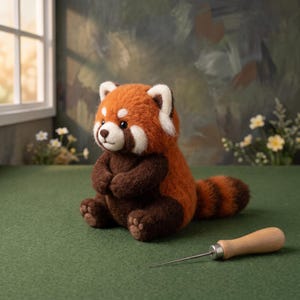 May include: A needle-felted red panda figurine with rust-orange and dark brown fur, white facial markings, and a striped tail, sitting upright. A wooden-handled metal awl tool is positioned on the surface next to the plush animal figure.