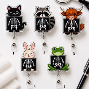 May include: Five acrylic badge reels featuring cartoon animals with visible skeletal X-ray designs. The characters include a black cat, a raccoon, a highland cow, a rabbit, and a green frog, each labeled with numbers one through five.