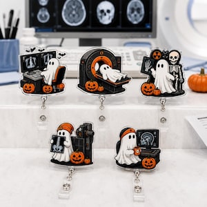 May include: Five acrylic badge reels featuring white ghosts in medical settings with orange pumpkins. One ghost works at a computer, one lies in an MRI machine, one holds an X-ray with a skeleton, one holds a spine X-ray, and one holds a mug at a computer.