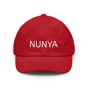 May include: A bright red baseball cap featuring the word NUNYA printed in white capital letters across the front center. The cap has a structured crown, a curved brim, and a button at the top, showcasing a classic six-panel design with stitching.