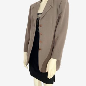 May include: A taupe blazer with a classic design, featuring a notched lapel and three brown buttons. The blazer is worn over a black dress with a lace top. The mannequin is on a white background.