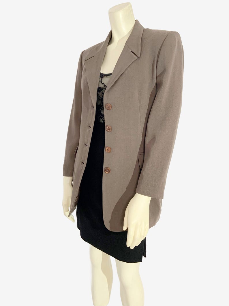May include: A taupe blazer with a classic design, featuring a notched lapel and three brown buttons. The blazer is worn over a black dress with a lace top. The mannequin is on a white background.