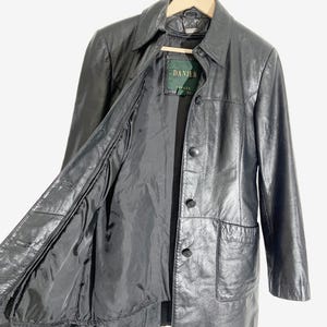 May include: Black leather jacket with a collared neckline, button closure, and two front pockets. The jacket is hanging on a wooden hanger. The interior lining is visible.