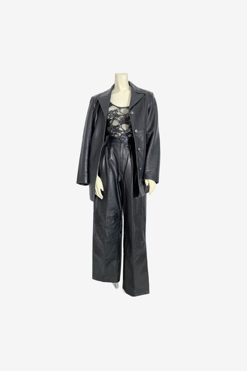 May include: A black leather blazer is draped over a mannequin wearing a black lace top and high-waisted, wide-leg leather trousers. The outfit is a monochromatic ensemble, showcasing a vintage fashion aesthetic.