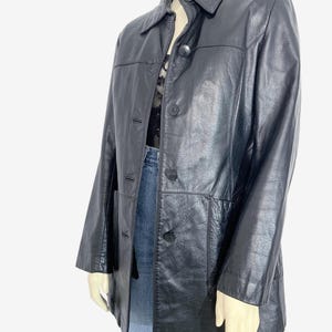 May include: A black leather jacket with a collared neckline and button-down closure. The jacket has long sleeves and two front pockets. The jacket is displayed on a mannequin.