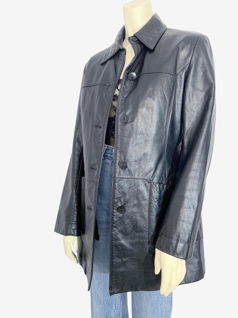 May include: A black leather jacket with a collared neckline and button-down closure. The jacket has long sleeves and two front pockets. The jacket is displayed on a mannequin.