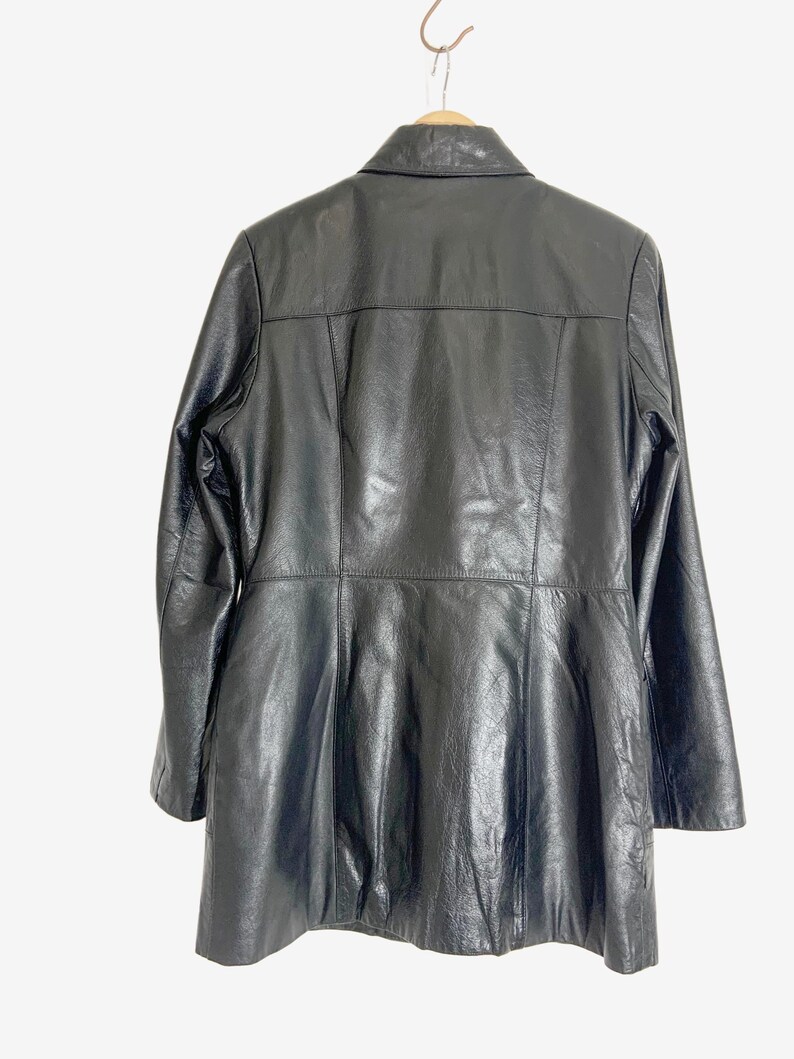 May include: Black leather jacket with a collared neckline and long sleeves. The jacket is hanging on a wooden hanger. The back of the jacket has a tailored design with vertical seams and a flared bottom.