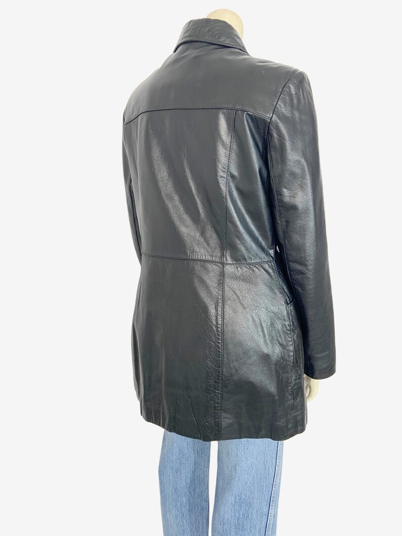 May include: A black leather jacket with a collared neckline and a tailored fit. The jacket has a button closure and a mid-thigh length. The back of the jacket features a horizontal seam across the upper back.