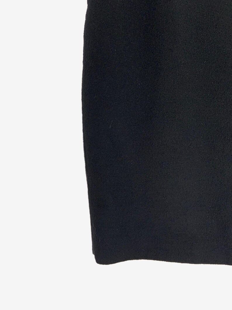 May include: A close-up shot of a black, textured fabric. The fabric appears to be a thick material, possibly wool or a similar textile. The image is well-lit, highlighting the texture and color of the material.