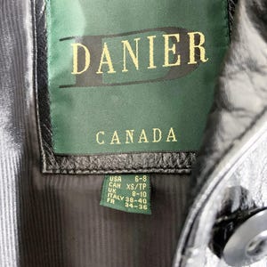 May include: Close-up of a black leather jacket's interior, showcasing a green tag with the brand name "DANIER" and "CANADA" in gold lettering. The tag also includes size conversions for USA, UK, Italy, and France.