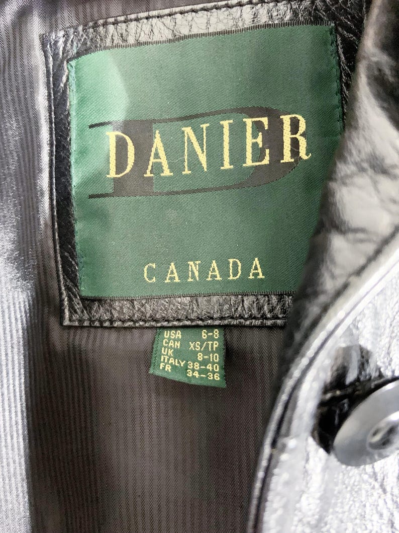 May include: Close-up of a black leather jacket's interior, showcasing a green tag with the brand name "DANIER" and "CANADA" in gold lettering. The tag also includes size conversions for USA, UK, Italy, and France.