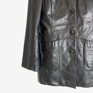 May include: Black leather jacket with three buttons and two front pockets. The jacket has a classic design with a slightly shiny finish. The sleeves are three-quarter length.