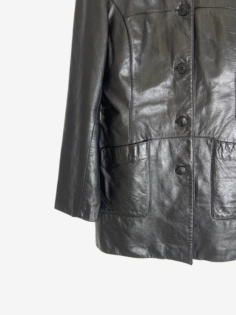 May include: Black leather jacket with three buttons and two front pockets. The jacket has a classic design with a slightly shiny finish. The sleeves are three-quarter length.