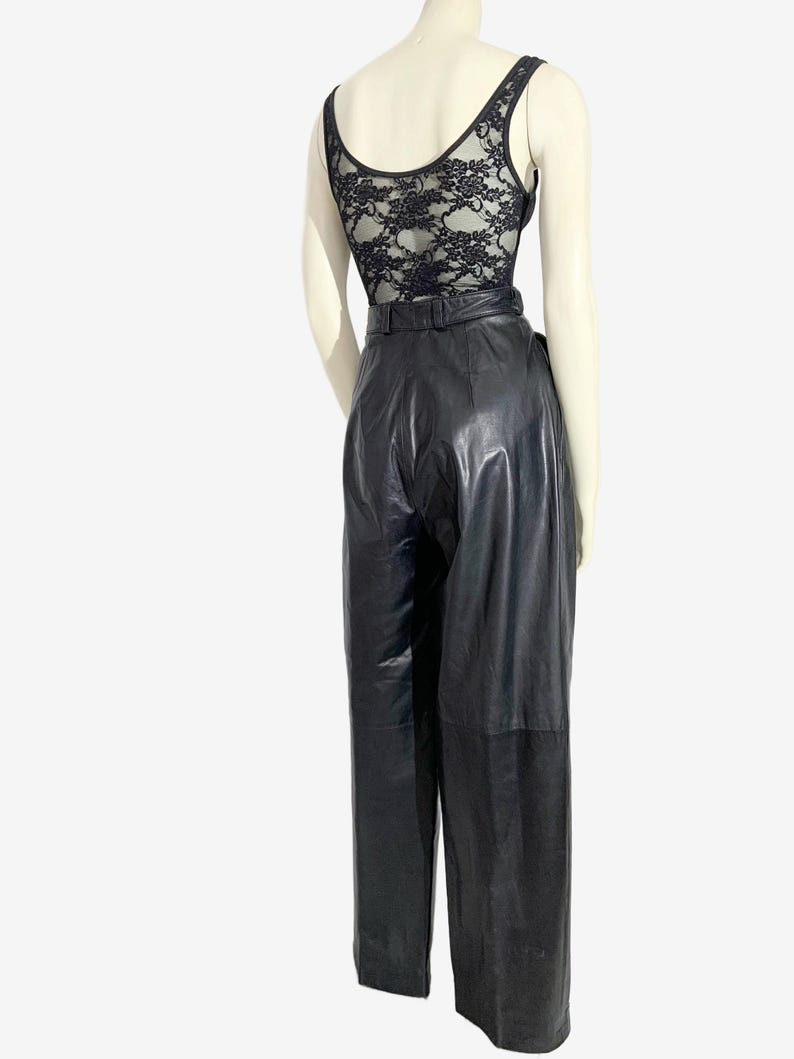 May include: A black lace bodysuit and high-waisted black leather trousers. The bodysuit has a scoop neck and a floral lace back. The trousers feature a belt and a straight-leg cut, creating a sleek, vintage-inspired outfit.
