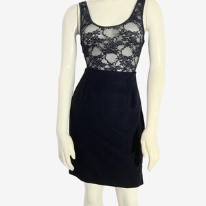 May include: A black dress on a mannequin. The top portion features a sheer black lace design over a solid black base. The skirt is a solid, dark black color. The dress has a scoop neckline and sleeveless design.