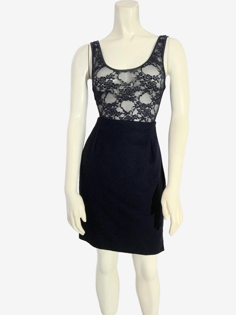 May include: A black dress on a mannequin. The top portion features a sheer black lace design over a solid black base. The skirt is a solid, dark black color. The dress has a scoop neckline and sleeveless design.