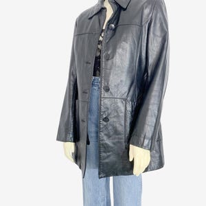 May include: Black leather jacket with a collared neckline and button-down closure. The jacket has two front pockets and is displayed on a mannequin. The jacket is a classic style, suitable for various occasions.