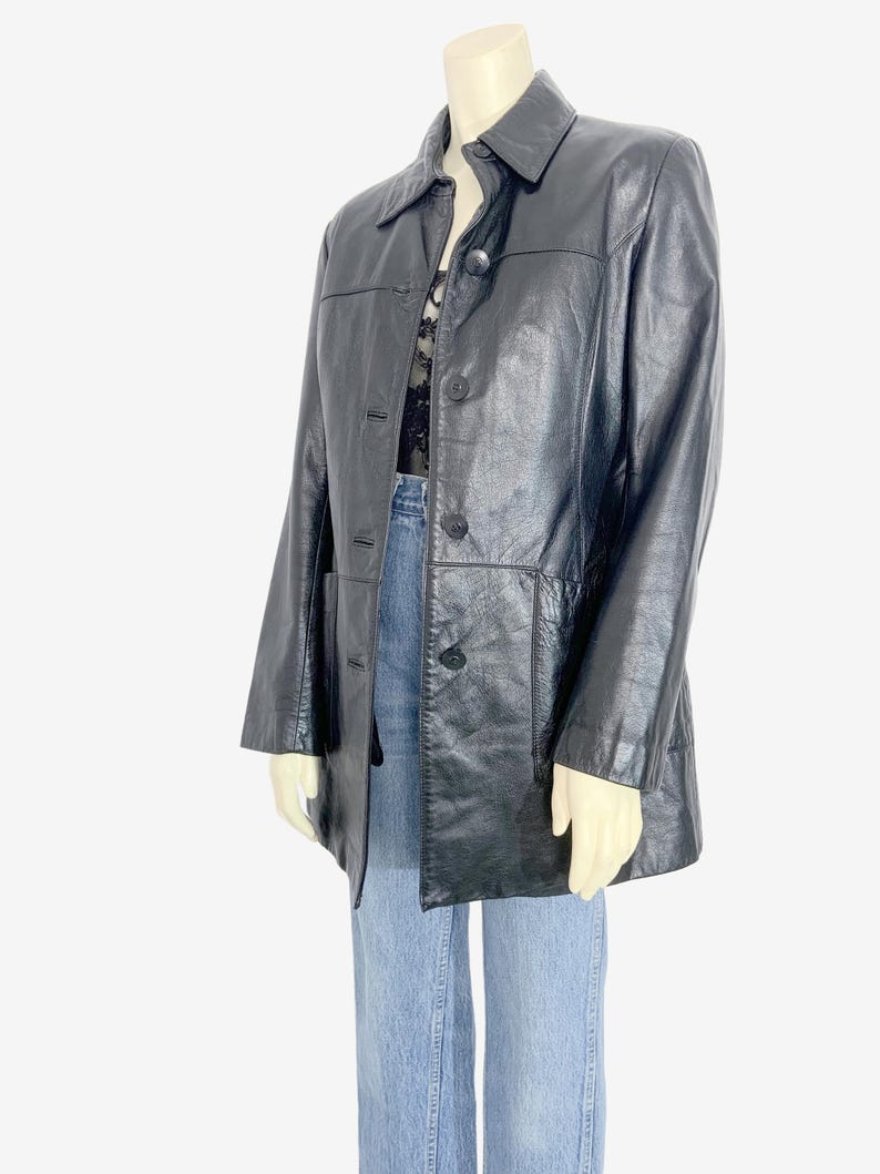 May include: Black leather jacket with a collared neckline and button-down closure. The jacket has two front pockets and is displayed on a mannequin. The jacket is a classic style, suitable for various occasions.