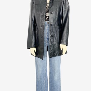 May include: A black leather jacket with a button-up front and a collared neckline. The jacket is paired with light blue denim jeans. The outfit is displayed on a mannequin.