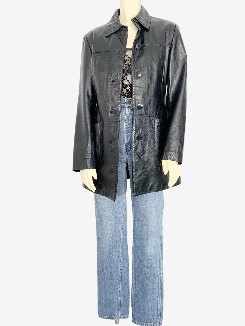 May include: A black leather jacket with a button-up front and a collared neckline. The jacket is paired with light blue denim jeans. The outfit is displayed on a mannequin.