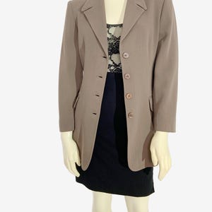 May include: A taupe blazer with a notched lapel and three-button closure. The blazer is worn over a black dress with a lace top. The mannequin is wearing a black skirt. The blazer has two front pockets.