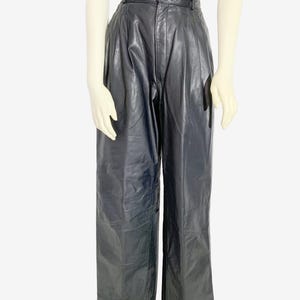 May include: Black leather trousers with a high waist and wide legs. The trousers have a button closure and pleats at the waist. The model is wearing a black lace top.