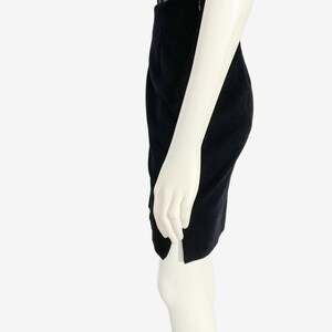 May include: A black pencil skirt with a side slit, paired with a black lace top. The skirt is knee-length and appears to be made of a soft fabric. The mannequin is white.