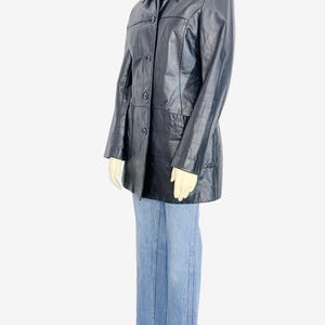 May include: A black leather jacket with a collared neckline and button-down closure. The jacket is paired with light blue denim jeans. The jacket has a classic, tailored design, and the jeans have a straight leg fit.