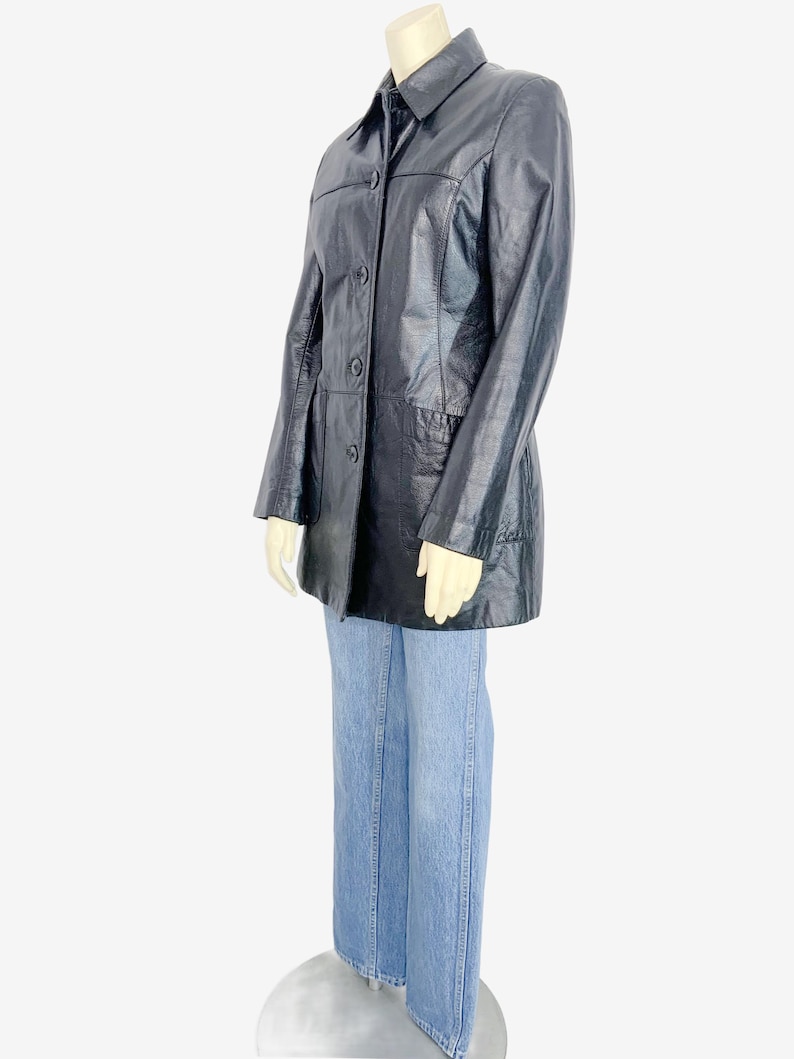 May include: A black leather jacket with a collared neckline and button-down closure. The jacket is paired with light blue denim jeans. The jacket has a classic, tailored design, and the jeans have a straight leg fit.