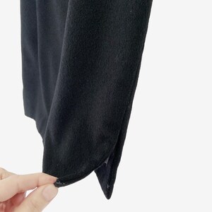 May include: Close-up of a black fabric with a soft texture. The fabric is folded, revealing a curved edge and a small slit. The image is set against a white background.
