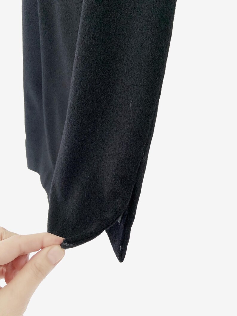 May include: Close-up of a black fabric with a soft texture. The fabric is folded, revealing a curved edge and a small slit. The image is set against a white background.