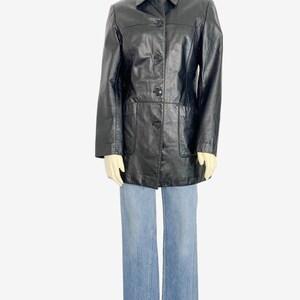 May include: A black leather jacket with a collared neckline, button-down front, and two front pockets. The jacket is paired with light blue denim jeans. The jacket appears to be a vintage style.