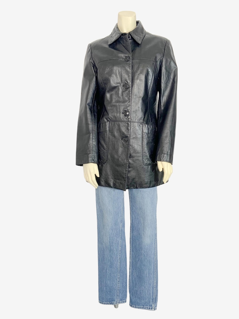 May include: A black leather jacket with a collared neckline, button-down front, and two front pockets. The jacket is paired with light blue denim jeans. The jacket appears to be a vintage style.