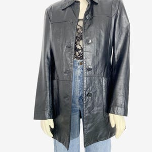 May include: A black leather jacket with a collared neckline and button-down closure. The jacket has a classic design with a tailored fit, featuring pockets and a mid-length cut. The jacket is displayed on a mannequin.