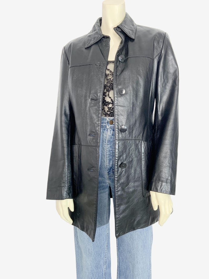 May include: A black leather jacket with a collared neckline and button-down closure. The jacket has a classic design with a tailored fit, featuring pockets and a mid-length cut. The jacket is displayed on a mannequin.