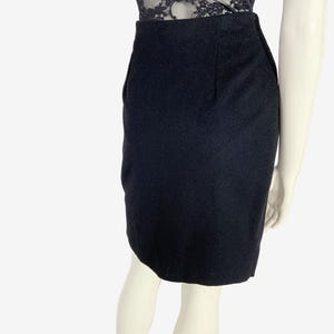 May include: A black pencil skirt made of a textured fabric. The skirt is knee-length and has a classic, tailored design. The skirt is shown on a mannequin, paired with a black lace top.