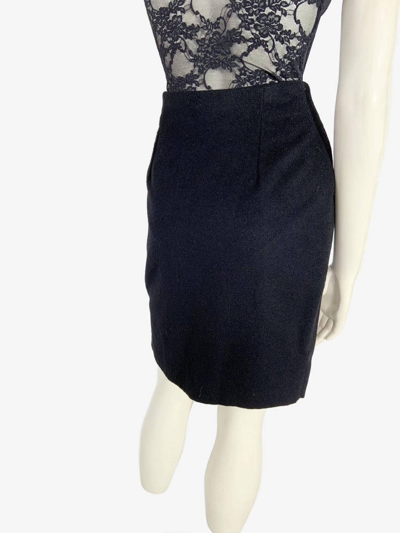 May include: A black pencil skirt made of a textured fabric. The skirt is knee-length and has a classic, tailored design. The skirt is shown on a mannequin, paired with a black lace top.