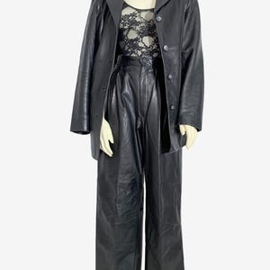 May include: A black leather outfit displayed on a mannequin. The ensemble features a long-sleeved blazer, high-waisted trousers, and a lace top. The blazer has a button closure and a notched collar. The trousers are wide-legged. The lace top is visible.