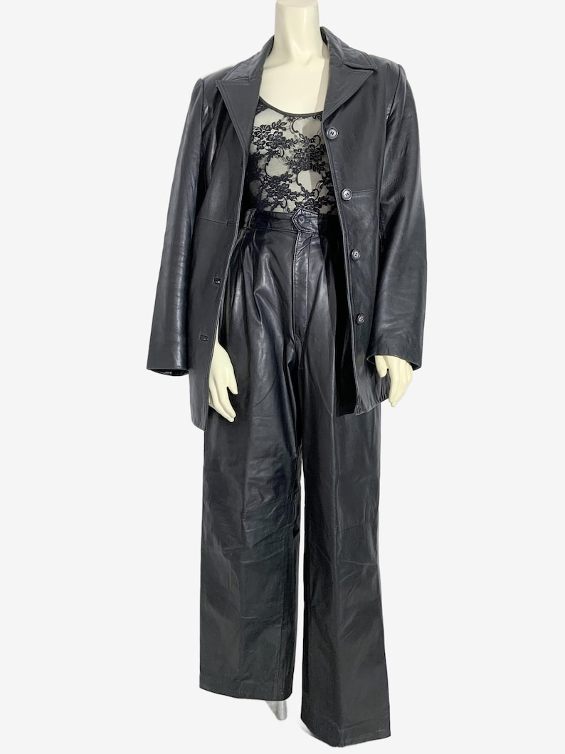 May include: A black leather outfit displayed on a mannequin. The ensemble features a long-sleeved blazer, high-waisted trousers, and a lace top. The blazer has a button closure and a notched collar. The trousers are wide-legged. The lace top is visible.