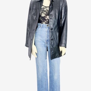 May include: A black leather jacket with a button-up front, worn over a black lace top and light blue denim jeans. The jacket has a collared neckline and long sleeves. The jeans are high-waisted with a wide leg.