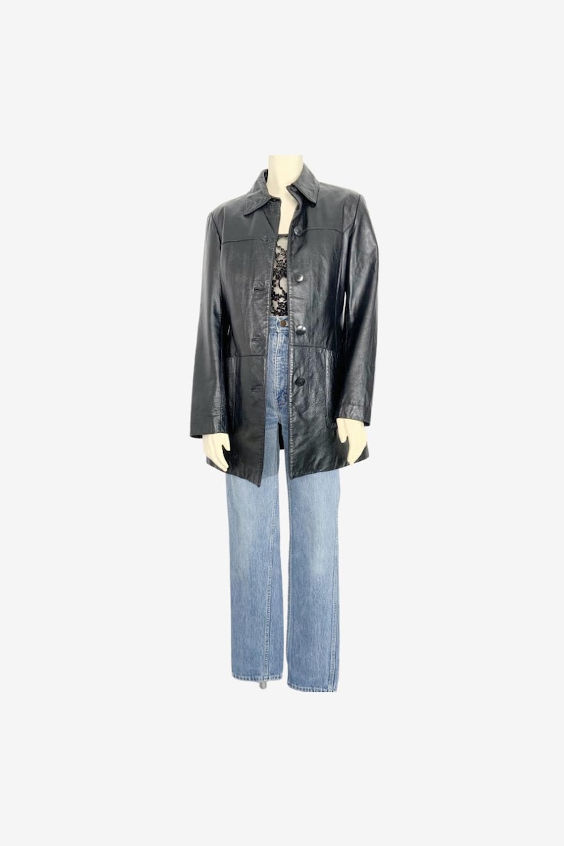 May include: A black leather jacket with a button-up front and a collared neckline. The jacket is paired with light blue denim jeans. The outfit is displayed on a mannequin against a white background.