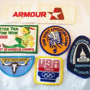 Peut inclure: Collection de patchs brodés vintage. Comprend un patch blanc avec "ARMOUR" en rouge, un patch Peter Pan, un patch Cub Scout, un patch Kansas Pacific Railway, un patch USA 1984 Olympics et un patch Jefferson National Expansion Memorial.