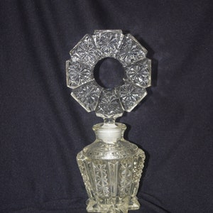 Pu&ograve; includere: Flacone di profumo in vetro trasparente con un design geometrico decorativo. La bottiglia ha un motivo a stella e un tappo circolare. La bottiglia &egrave; alta circa 13 cm.